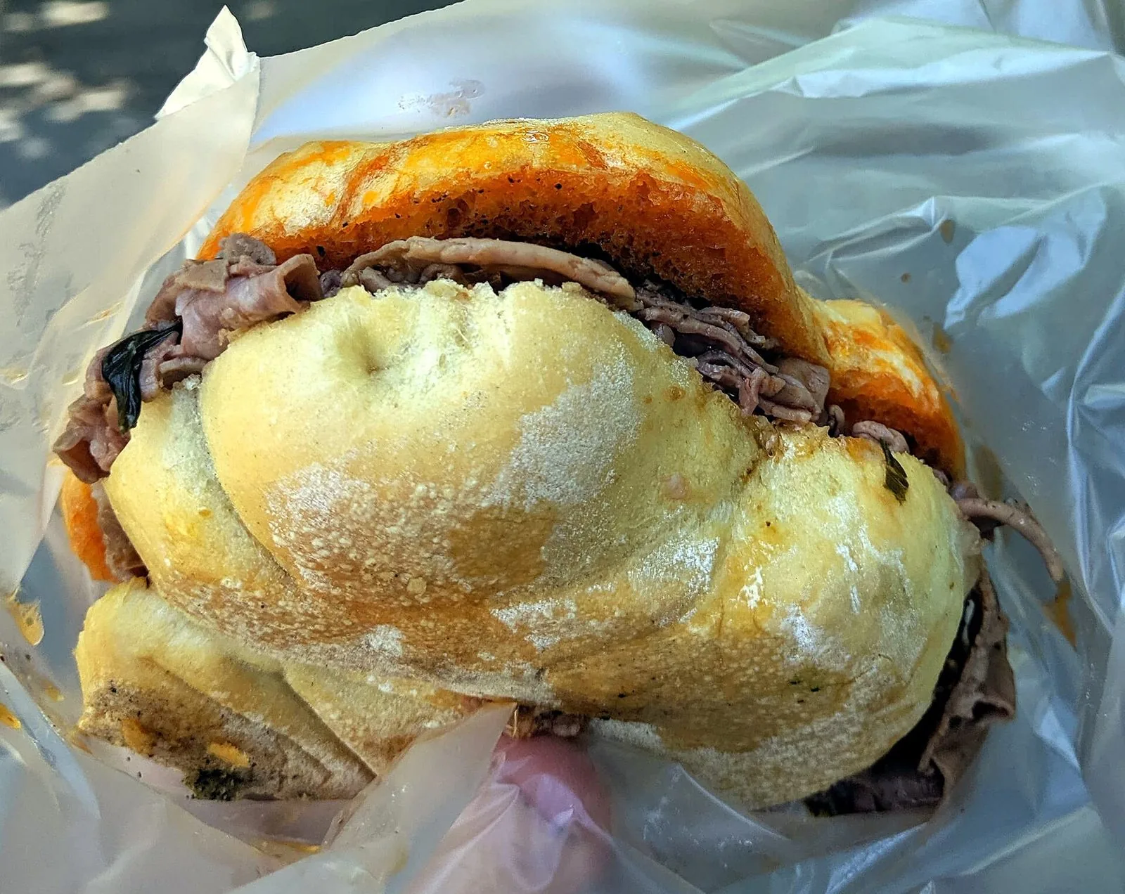 Un panino al lampredotto avvolto nella carta: la trippa tagliata a fettine sottili, la salsa verde e il pane con la parte superiore bagnata nel brodo di cottura