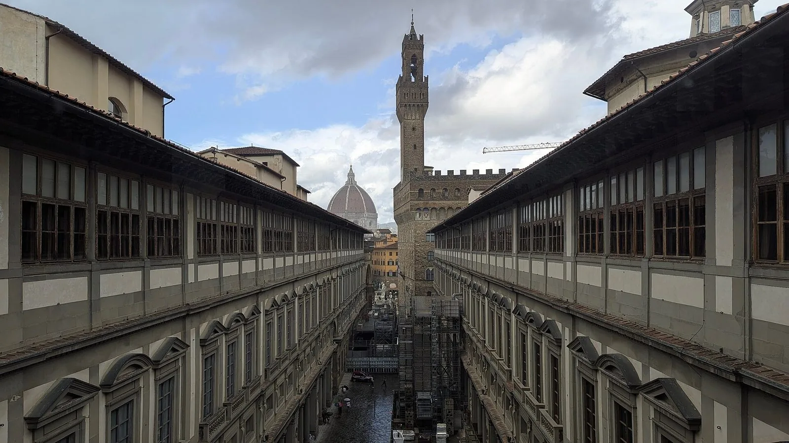 Il cortile degli Uffizi visto dall'alto, stretto tra le due lunghe ali porticate della galleria, con in fondo la torre di Palazzo Vecchio e la cupola del Duomo sotto un cielo nuvoloso