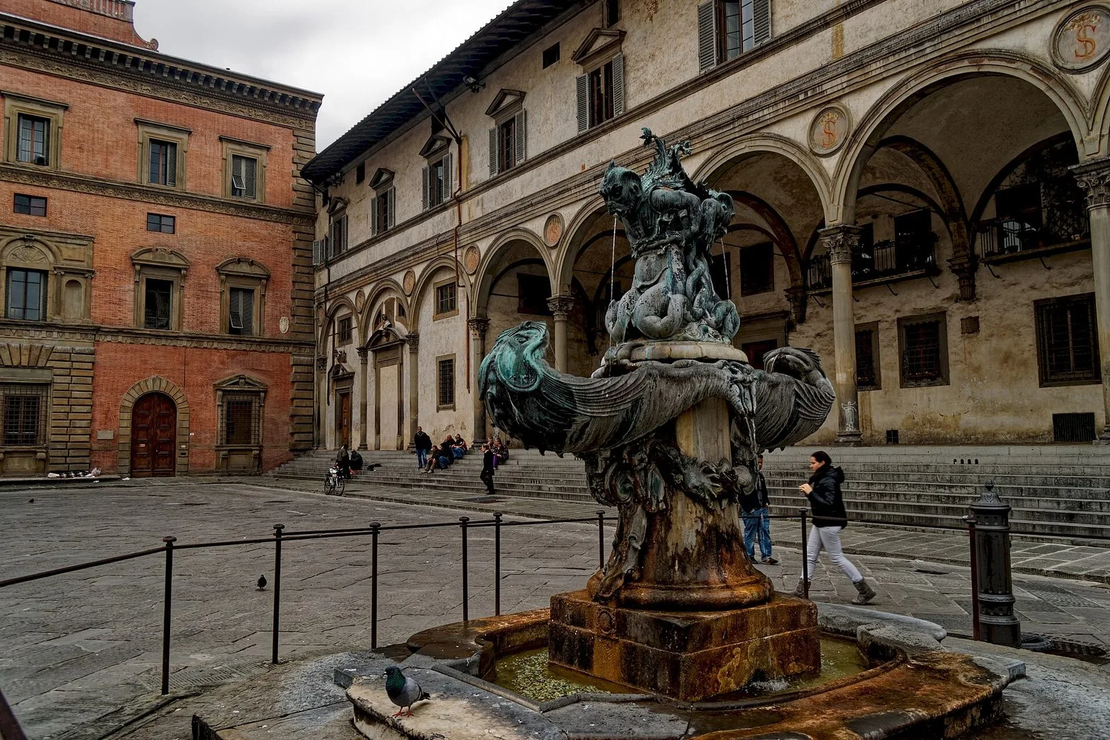 Una delle due fontane in bronzo di Pietro Tacca in Piazza della Santissima Annunziata, con mostri marini e vasche a conchiglia, e alle spalle il porticato ad archi dello Spedale degli Innocenti e un palazzo in mattoni